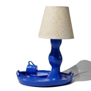 Niebieska lampa stołowa z kremowym tekstylnym abażurem.